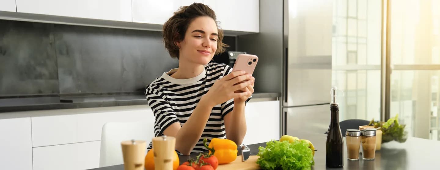 A person using a phone at a kitchen counter with fresh ingredients